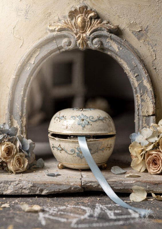 Affiche boîte à musique en porcelaine ouverte avec ruban bleu entourée de fleurs séchées dans décor vintage patiné