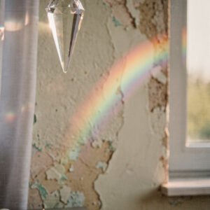 Affiche prisme en cristal suspendu projetant un arc-en-ciel sur un mur texturé éclairé par la lumière naturelle.