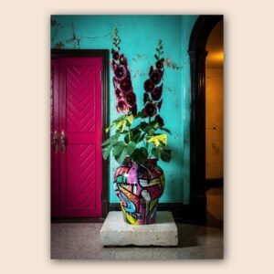 Affiche avec un vase coloré rempli de fleurs pourpres devant un mur turquoise patiné, une porte rose et une arche sombre.